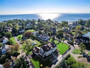 High-angle view of a residential neighborhood bordering a large body of water, showcasing various homes, lawns, and streets.