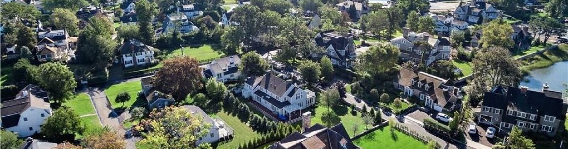 High-angle view of a residential neighborhood bordering a large body of water, showcasing various homes, lawns, and streets.